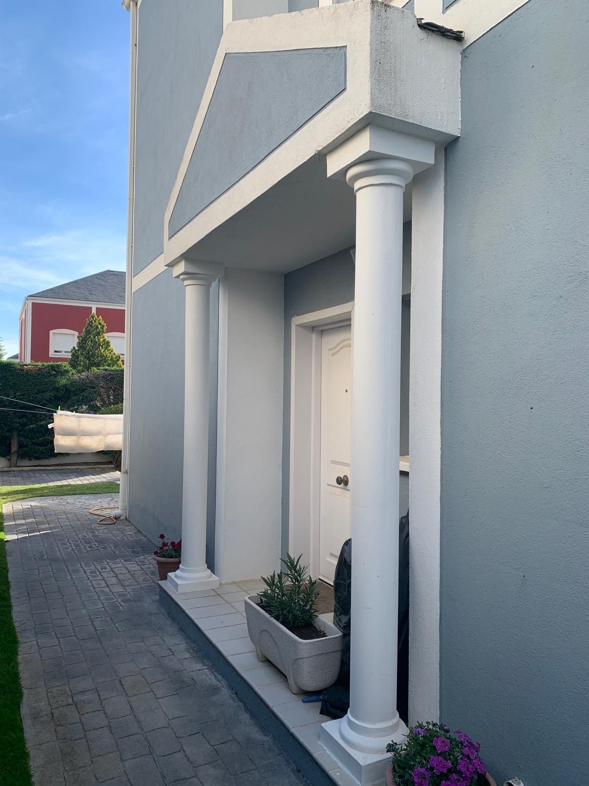 Una casa con un porche con columnas blancas y flores moradas.