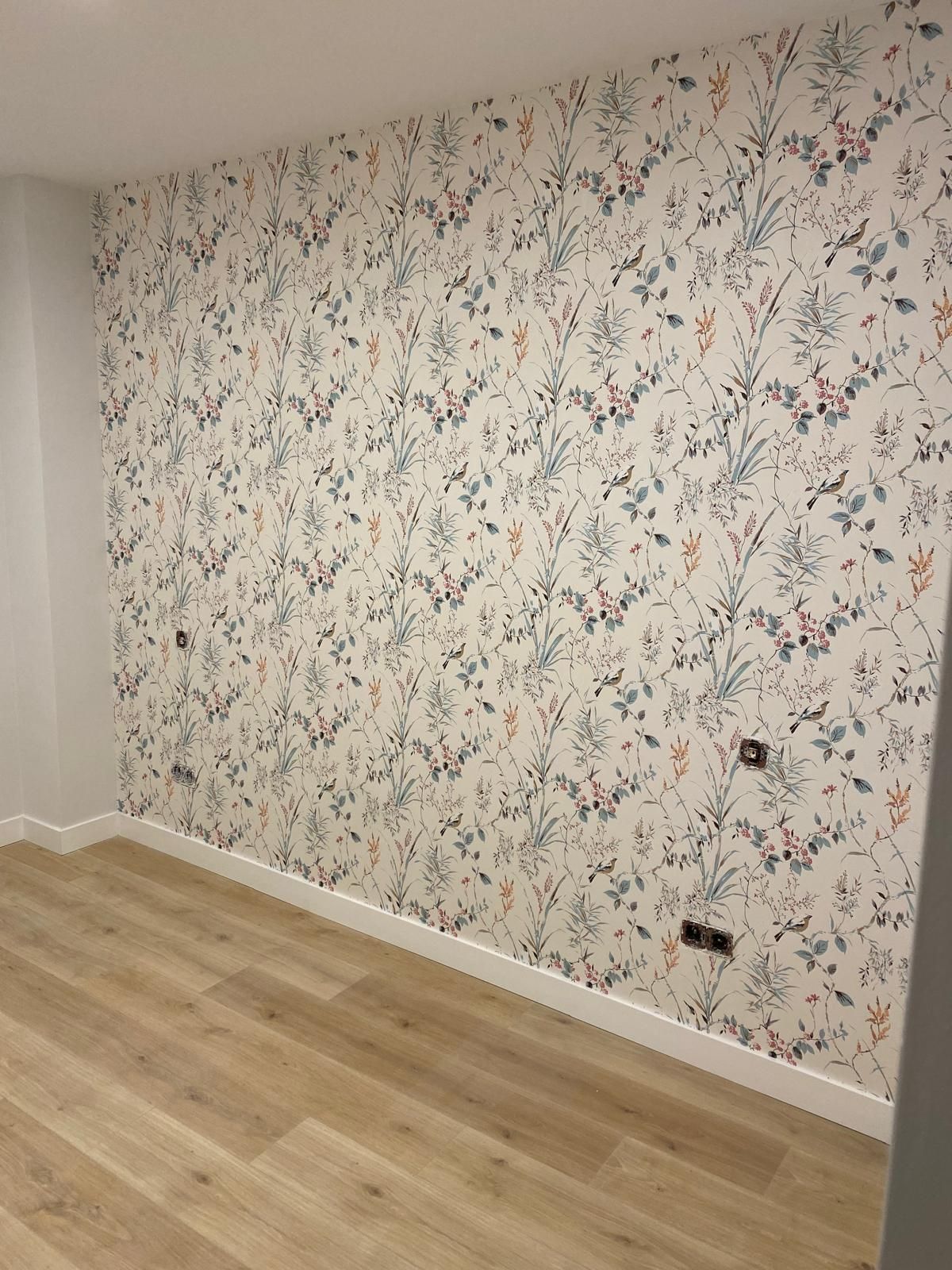 Una habitación con un papel pintado floral en la pared y un suelo de madera.