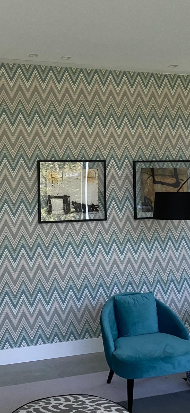 Una sala de estar con una silla azul, una mesa de café y un papel tapiz con estampado de chevrones.