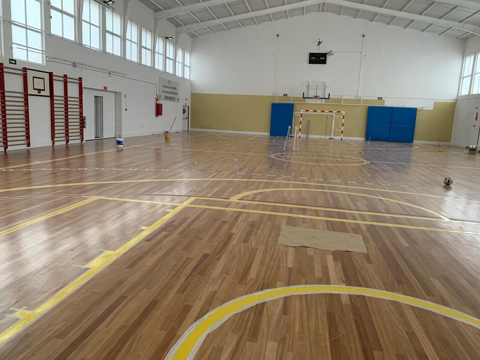 Un gimnasio vacío con suelo de madera y líneas amarillas.