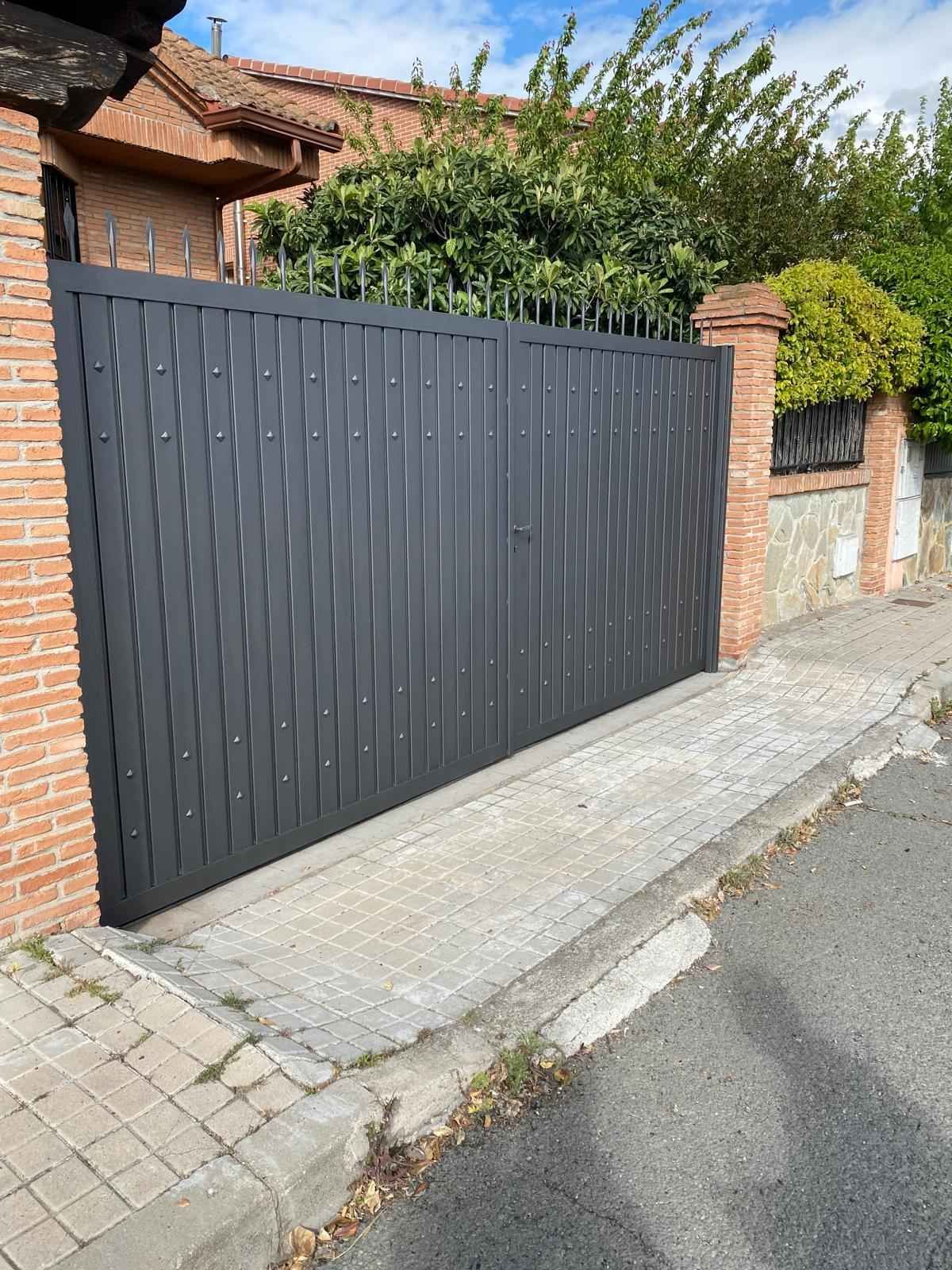 Una puerta negra está al costado de la carretera, al lado de una pared de ladrillos.