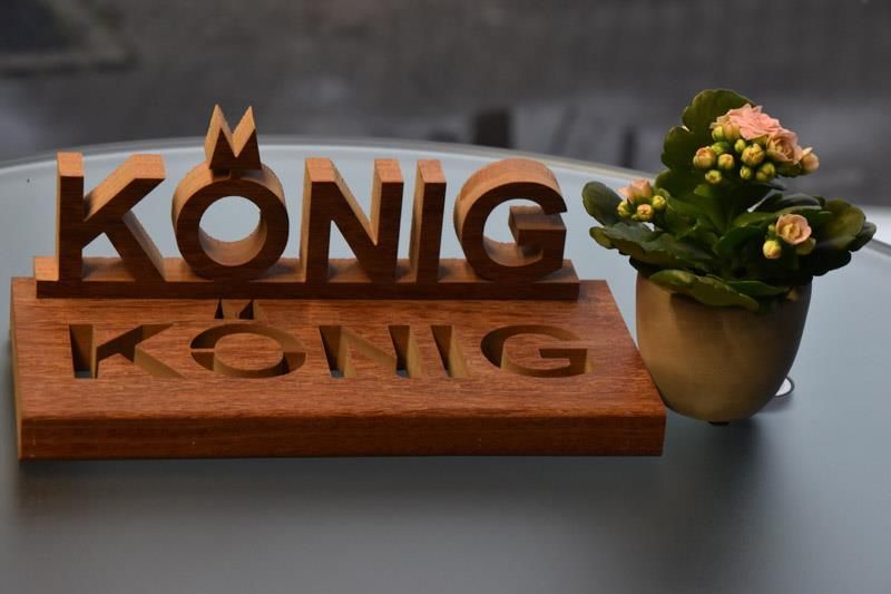 Ein Holzschild mit der Aufschrift „König Kong“ steht auf einem Tisch neben einer Topfpflanze