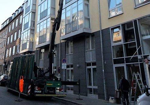 Vor einem Gebäude parkt ein LKW mit einem daran befestigten Kran.