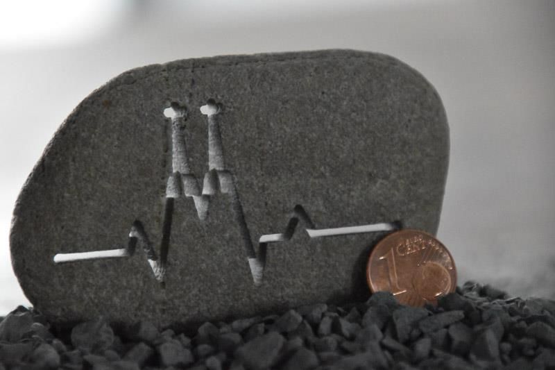Neben einem Stein liegt ein Penny, auf dem ein Herzschlag abgebildet ist.