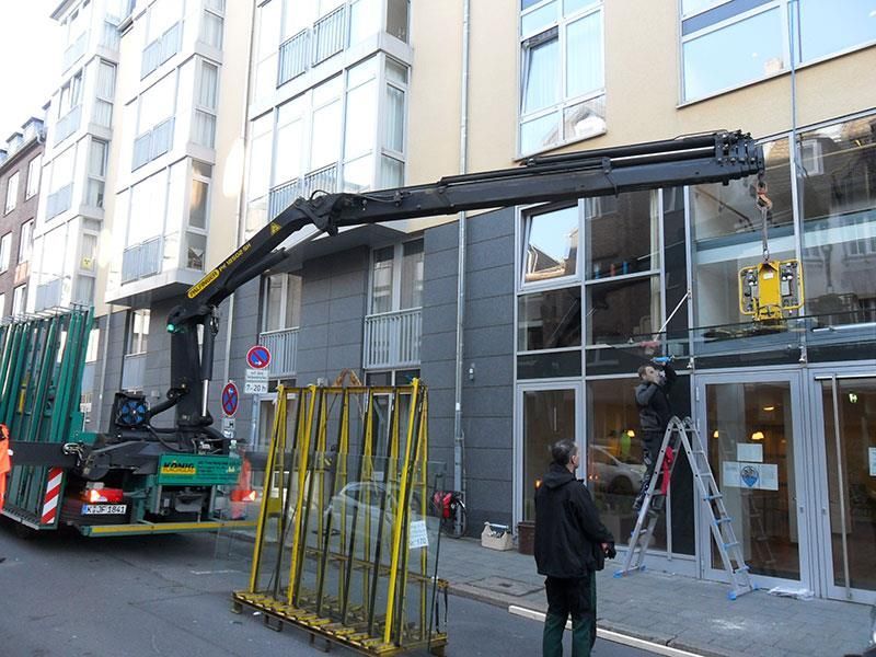 Ein Mann steht vor einem Gebäude, während ein Kran ein großes Stück Glas anhebt