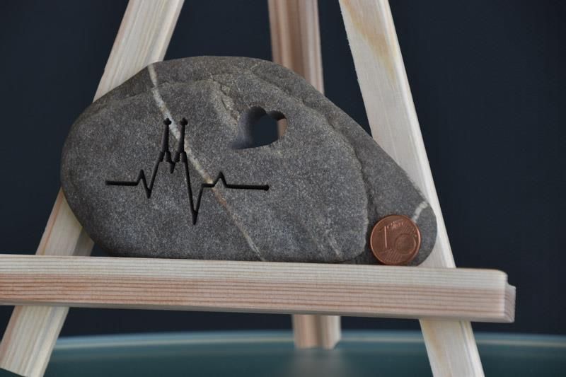 Ein Stein mit einem Herzschlag darauf liegt auf einer hölzernen Staffelei neben einem Penny