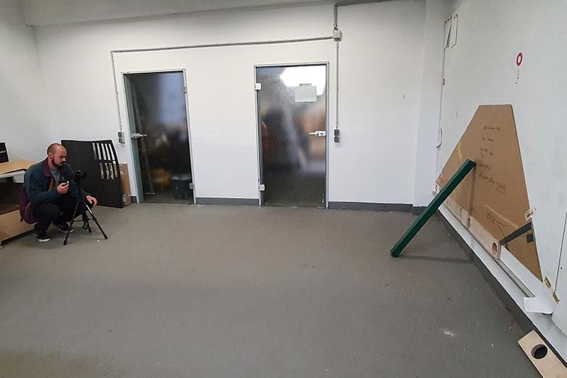 Ein Mann kniet mit einer Kamera in einem leeren Raum.