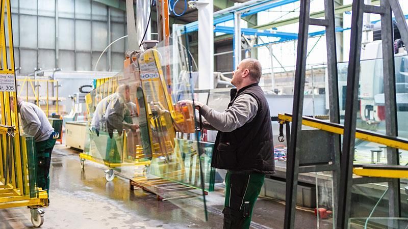 Ein Mann hebt in einer Fabrik ein großes Stück Glas hoch.