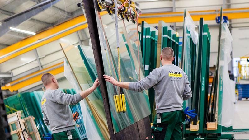 Zwei Männer arbeiten in einer Fabrik an einem großen Stück Glas.