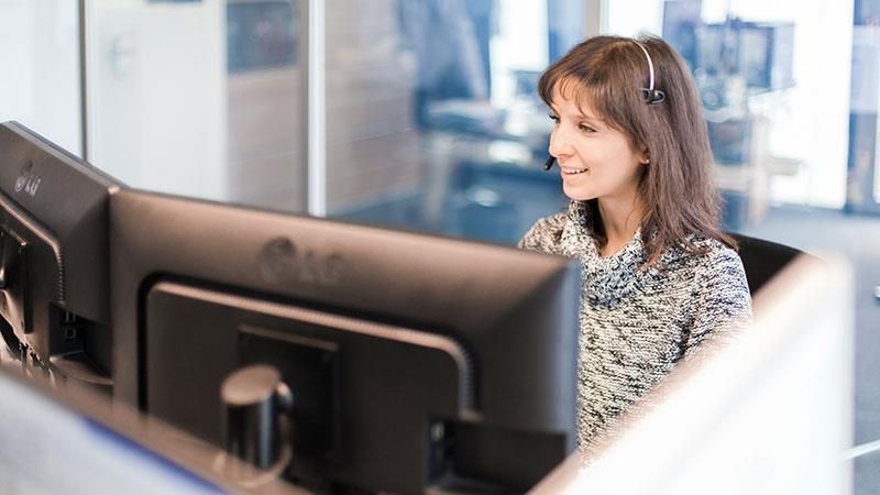 Eine Frau mit Headset sitzt vor einem Computermonitor.