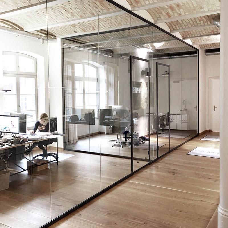 Eine Frau sitzt an einem Schreibtisch in einem Büro mit Glaswänden.