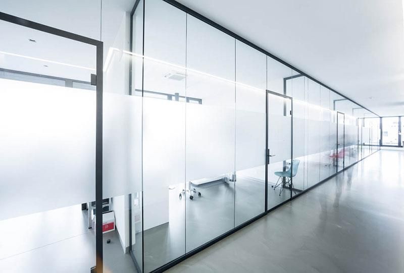 Ein langer Flur mit Glaswänden und -türen in einem Bürogebäude.