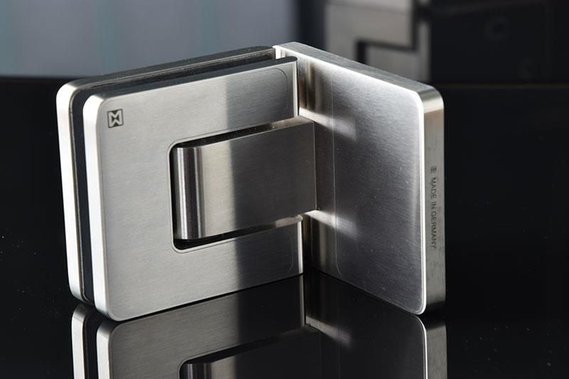 Auf einer schwarzen Fläche sitzt ein Türscharnier aus Edelstahl.