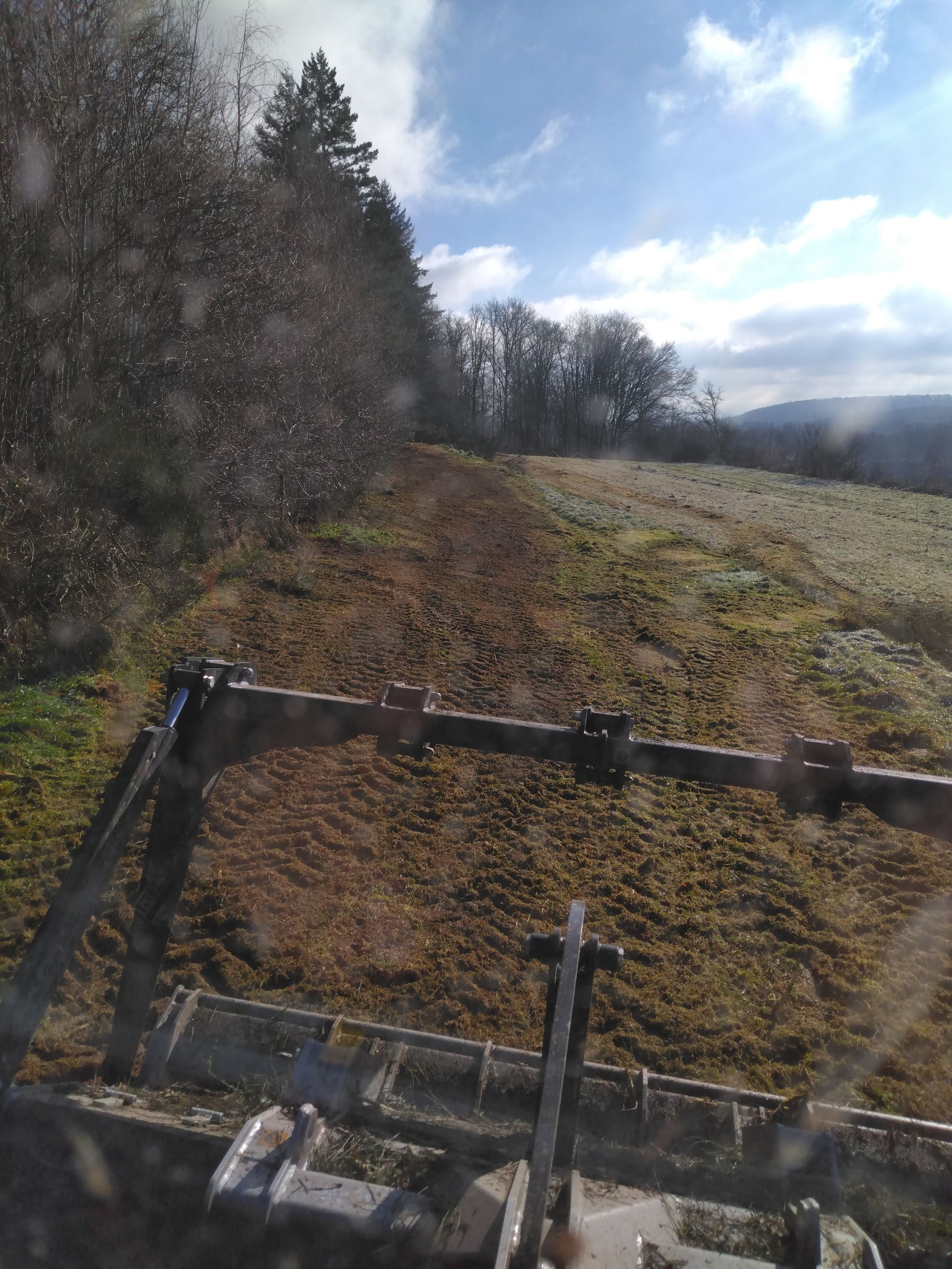 Un tracteur laboure un champ bordé d'arbres par une journée ensoleillée.