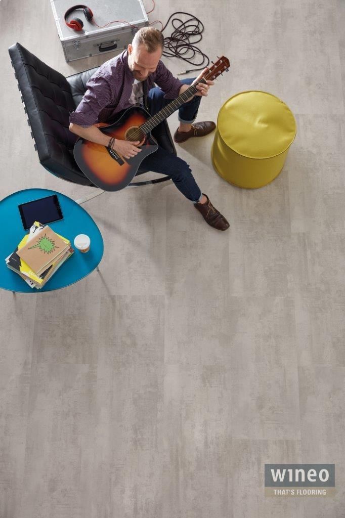 Dürr Stuckateure GmbH & Co.KG – Sicht von oben, Mann sitzt mit Gitarre auf einem Stuhl, grauer Boden.