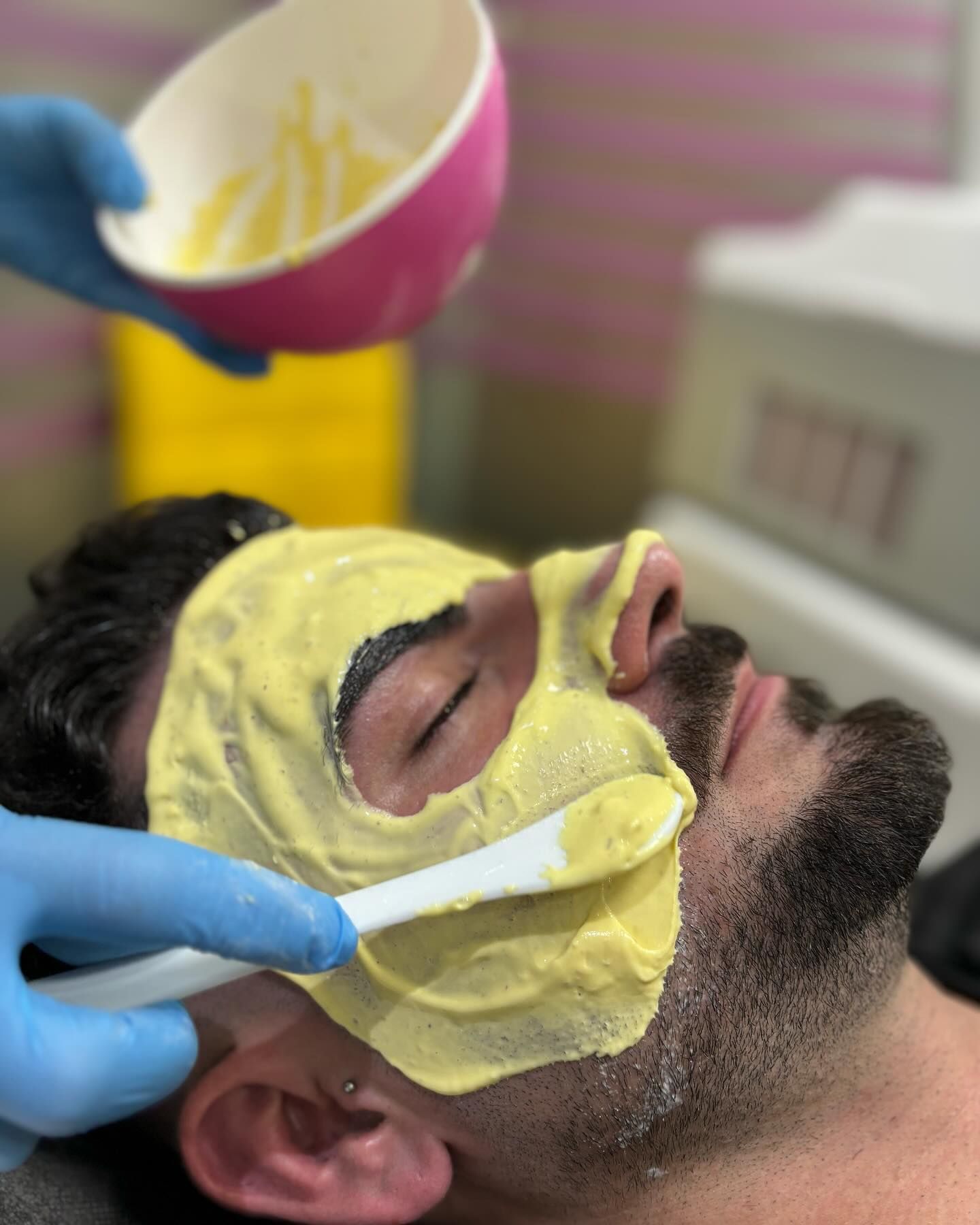 Persona que recibe un tratamiento facial: una máscara de color amarillo claro que se aplica en su cara con una espátula.