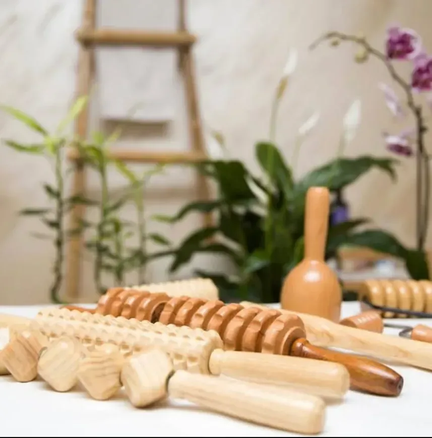 Herramientas de masaje de madera dispuestas sobre una superficie blanca con plantas y una escalera al fondo.