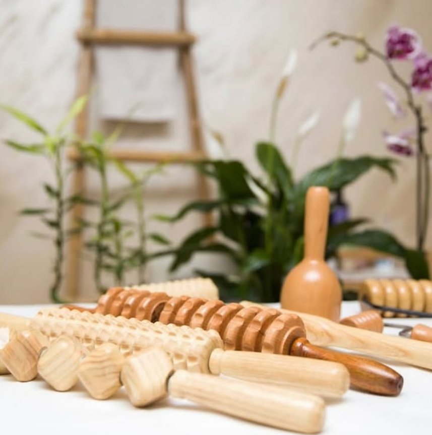 Mano de una persona que utiliza una herramienta de madera para masajear el abdomen de una persona acostada.