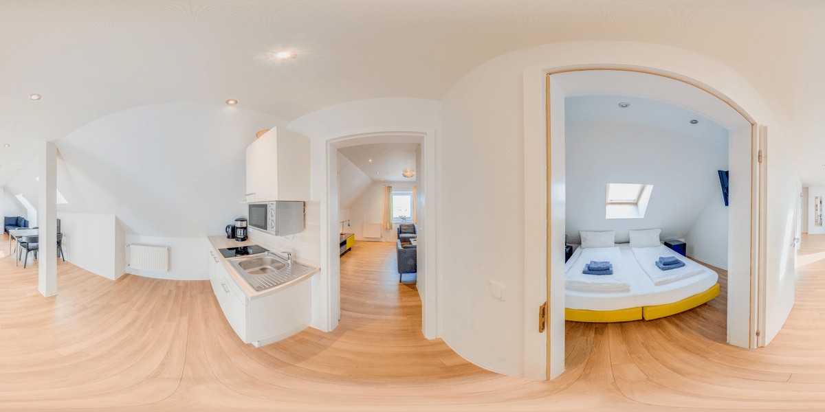 360-Grad-Ansicht einer lichtdurchfluteten Wohnung. Küchenbereich links, Schlafzimmer mit Doppelbett rechts.