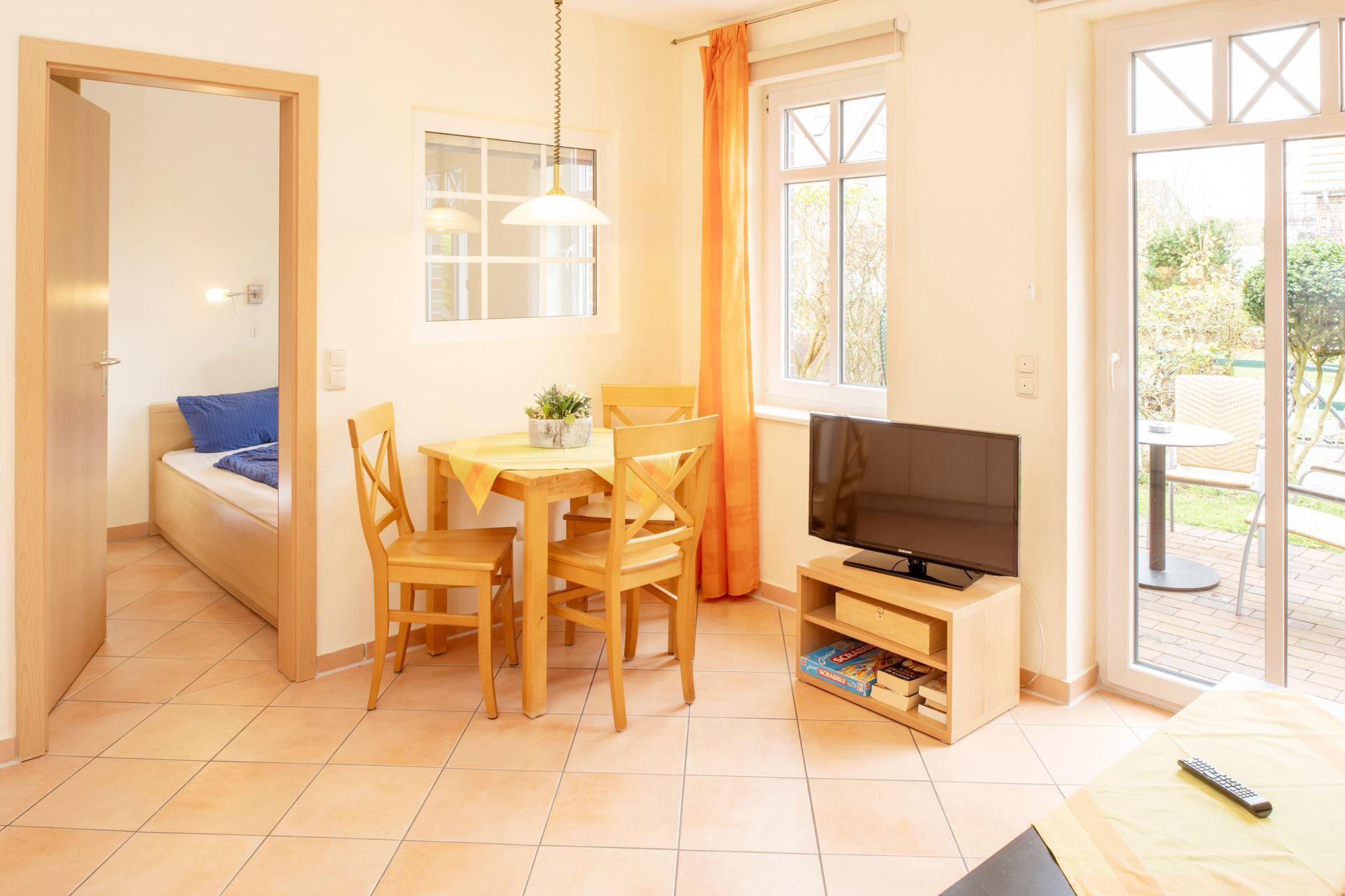 Wohnzimmer mit Esstisch, Fernseher und offener Tür zum Schlafzimmer und zur Terrasse.