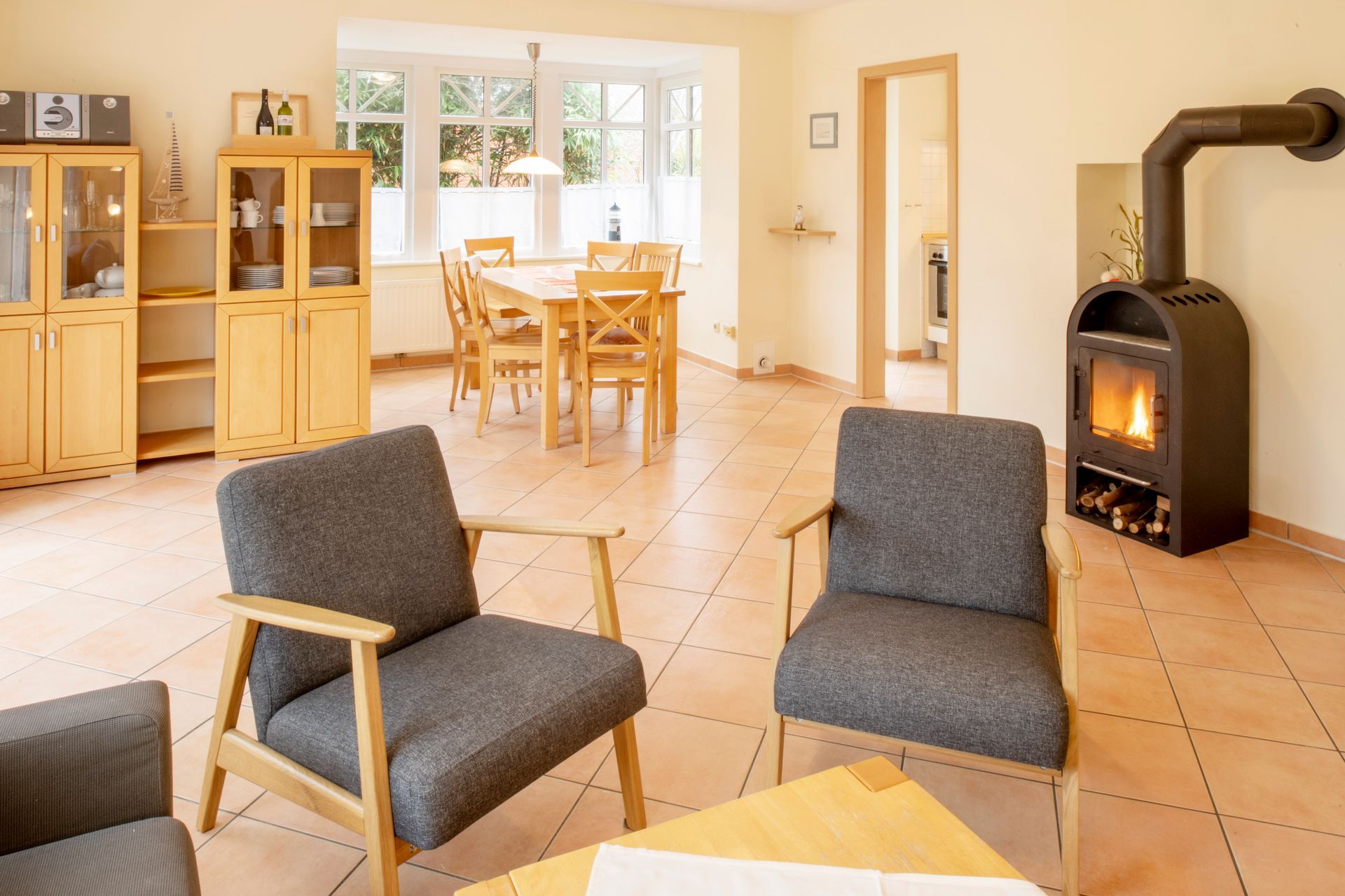 Wohnzimmer mit Stühlen, Kamin, Esstisch und hellen Holzschränken.