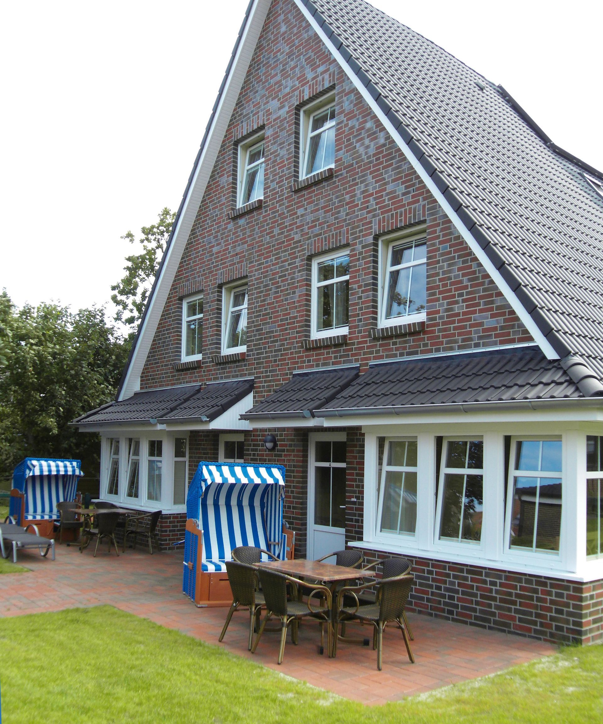 Backsteinhaus mit großem Giebeldach, weiß umrandeten Fenstern und Sitzgelegenheiten im Freien.