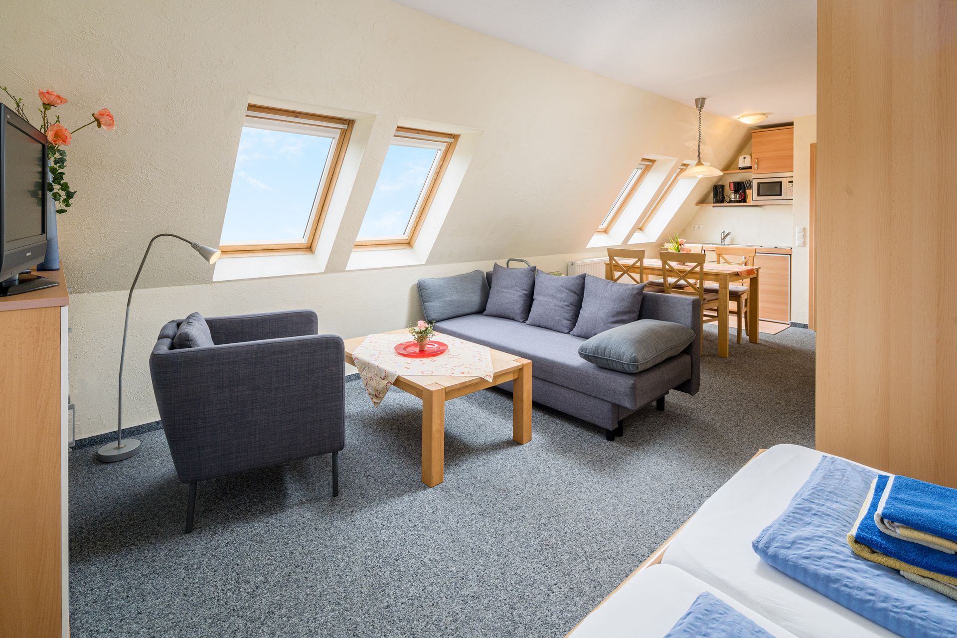 Gemütliches Apartmentinterieur mit Sofa, Sessel, Dachfenstern und einer kleinen Küche.