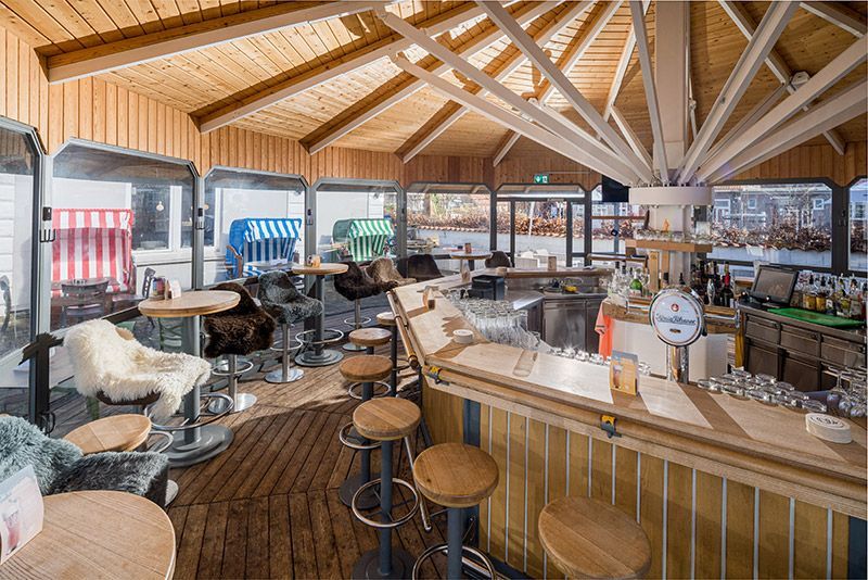 Café mit rotem Sonnenschirm, Strandstühlen, Fahrrädern und dem Schild „Info Cafe“ unter blauem Himmel.