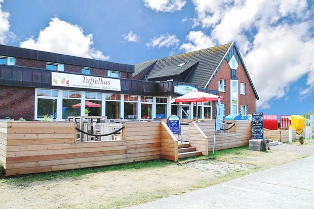 Restaurant mit Außenterrasse. Das Gebäude ist aus Ziegeln und Holz. Strahlender Himmel.