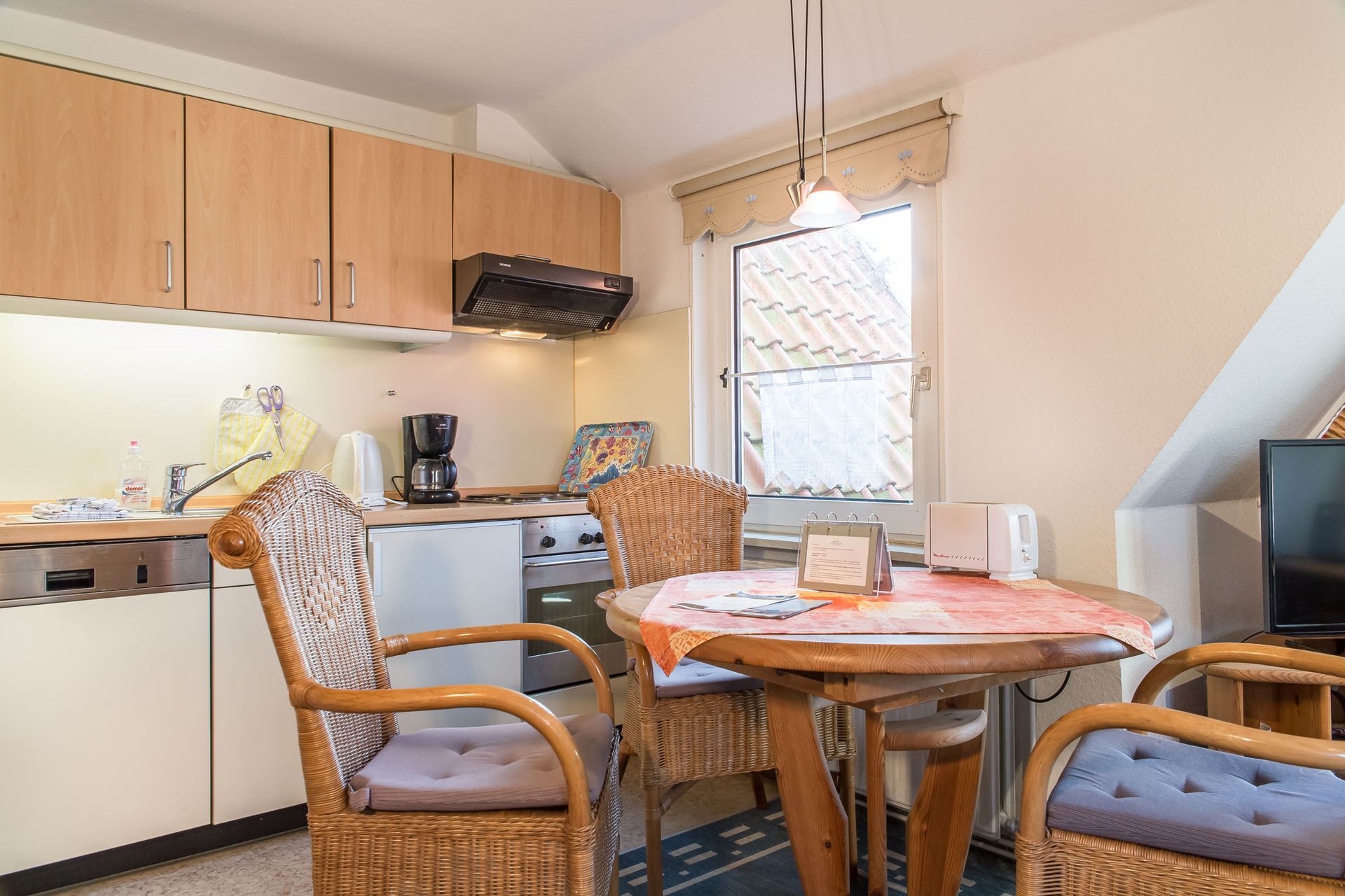 Kleine Küche und Essbereich mit Schränken, Geräten, Tisch und Stühlen.