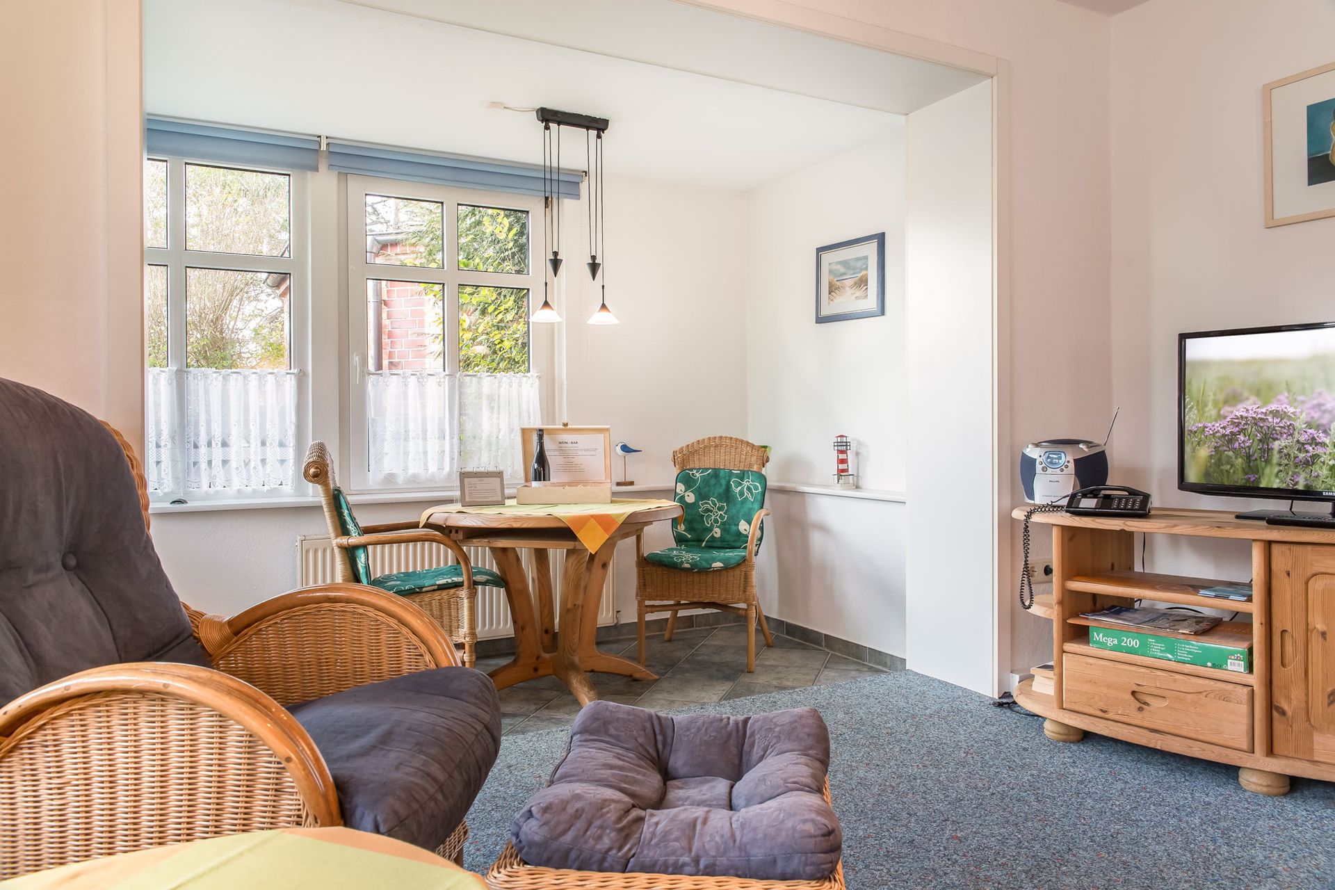 Wohnzimmer mit Korbmöbeln, kleiner Essgruppe, Fernseher auf einem Holzschrank und einem Fenster.