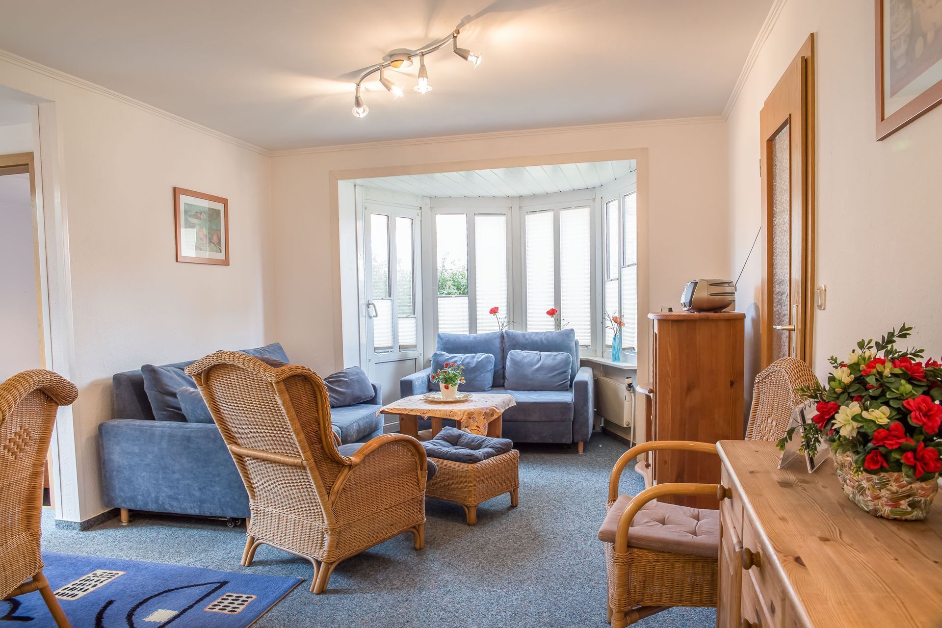 Wohnzimmer mit blauem Sofa, Korbmöbeln und Erkerfenster.