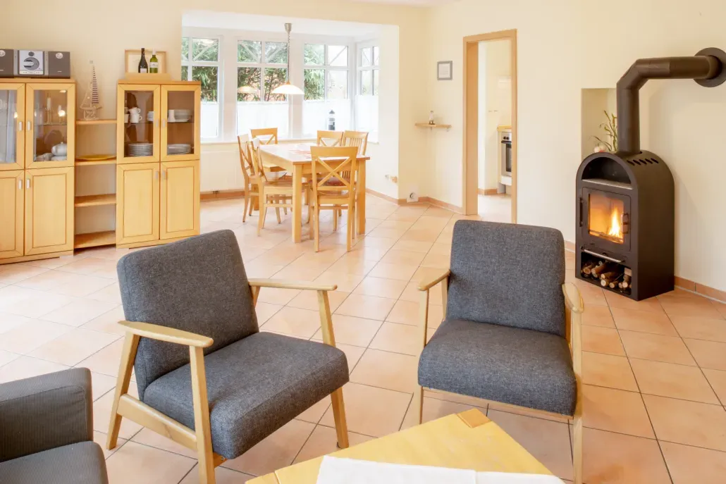 Wohnzimmer mit Kamin, Sesseln, Esstisch und Holzschränken; neutrale Farbpalette.