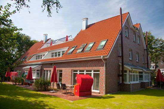 Hotel aus rotem Backstein mit weißen Verzierungen, rotem Dach und Balkonen in Küstenlage.