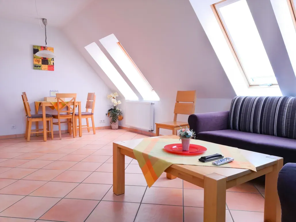 Wohnzimmer mit Esstisch, lila Sofa, Dachfenstern und hölzernem Couchtisch.