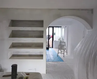 Une pièce inachevée avec des murs blancs et une fenêtre. Une échelle se trouve dans un coin.