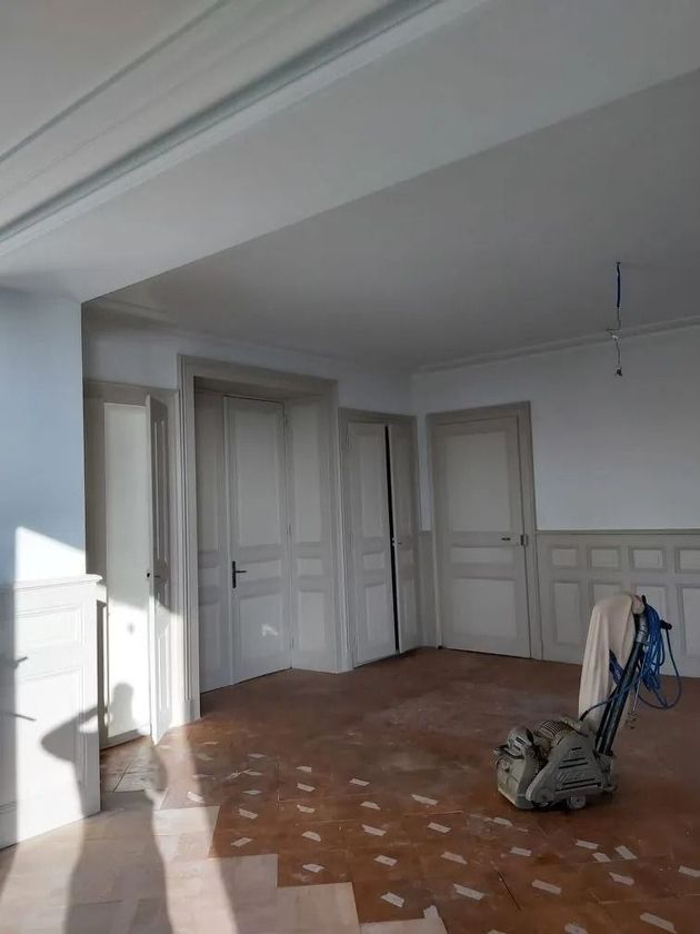 Pièce vide aux murs, portes et plafond blancs. Parquet marron, soleil et ponceuse à parquet.