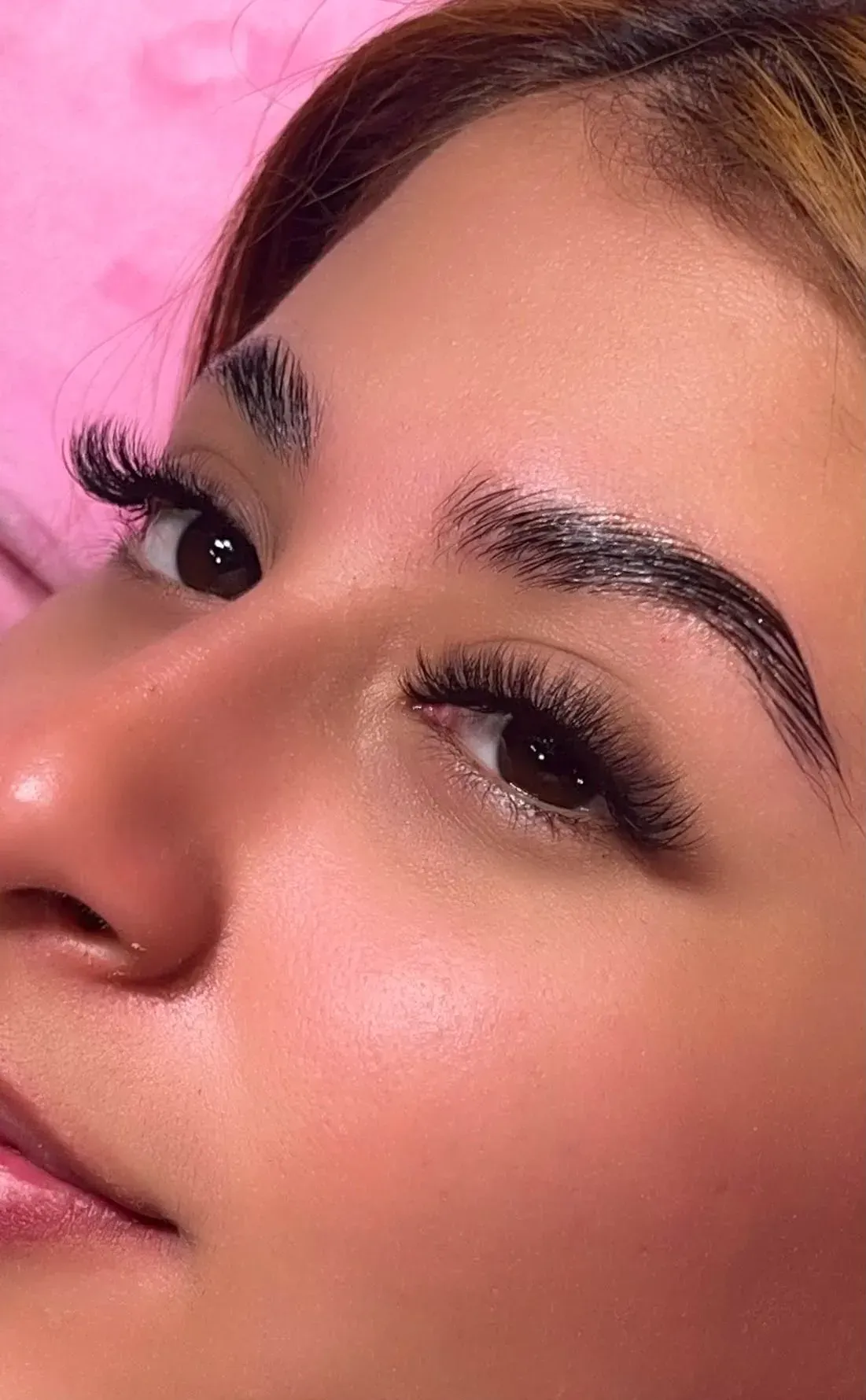 Primer plano de un rostro sonriente con largas pestañas sobre un fondo rosa.