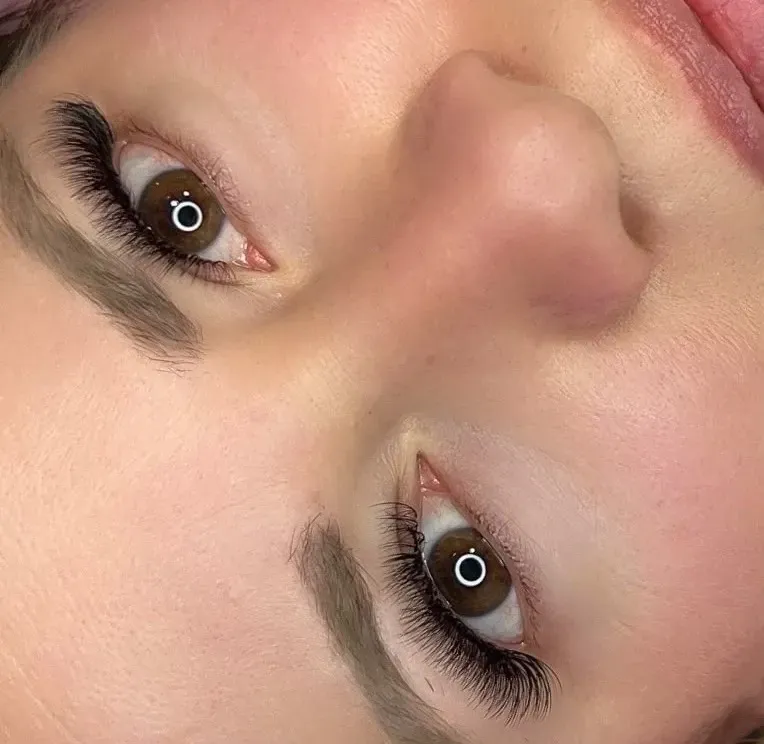 Primer plano de un rostro girado de lado, mostrando ojos marrones con pestañas largas y cejas definidas.