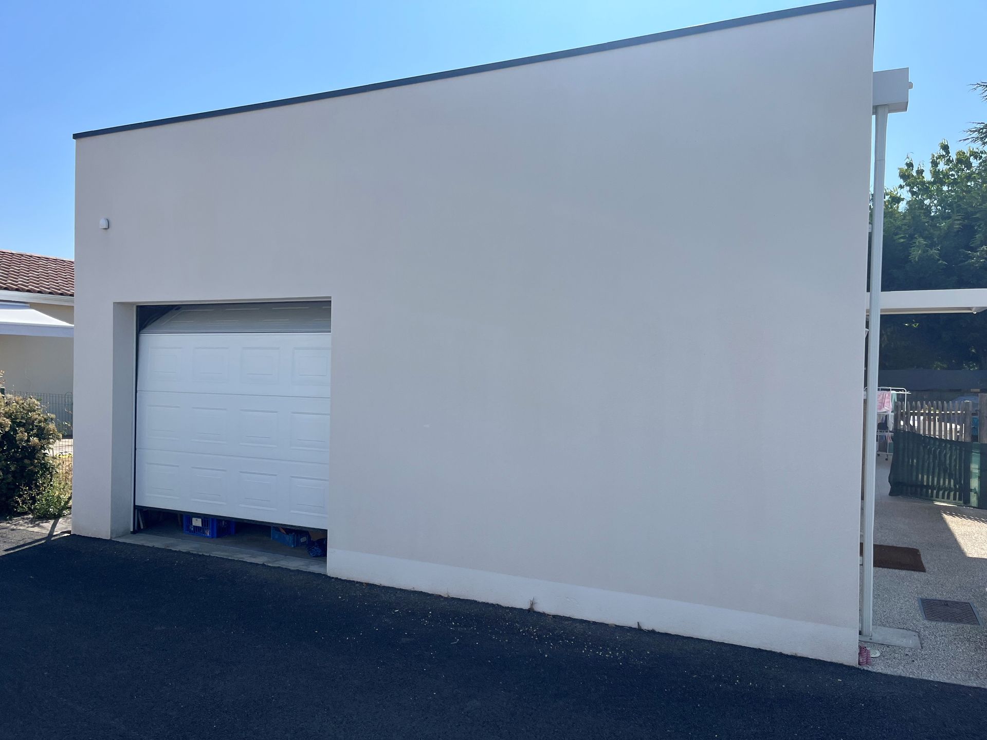 Façade de garage simple, de couleur claire, situé à côté d'une allée pavée sous un ciel bleu dégagé.