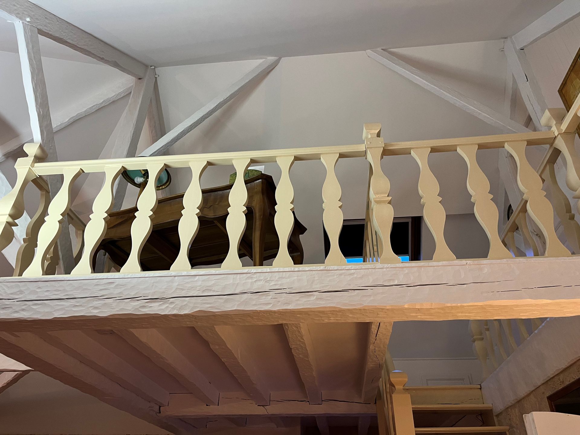 Vue intérieure d'un loft en bois avec une balustrade couleur crème donnant sur une pièce aux poutres apparentes au plafond.