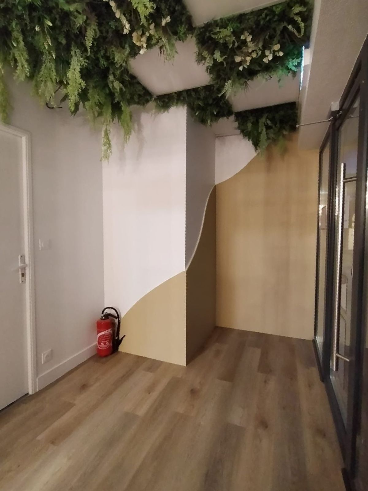 Un couloir avec un sol imitation bois, des murs peints d'un motif incurvé beige et blanc, des plantes vertes au plafond et un feu.