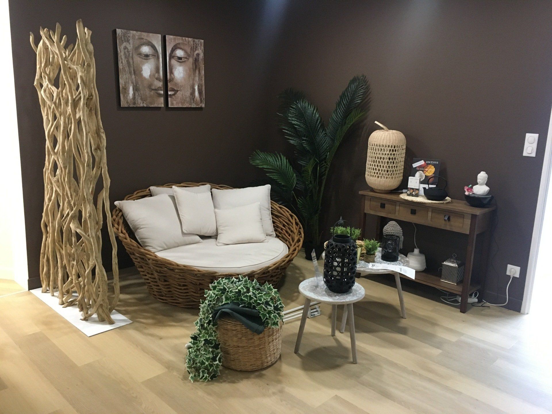 Un coin salon confortable comprenant un canapé rond en osier, un paravent en bois texturé, deux petites tables d'appoint et une console en bois.