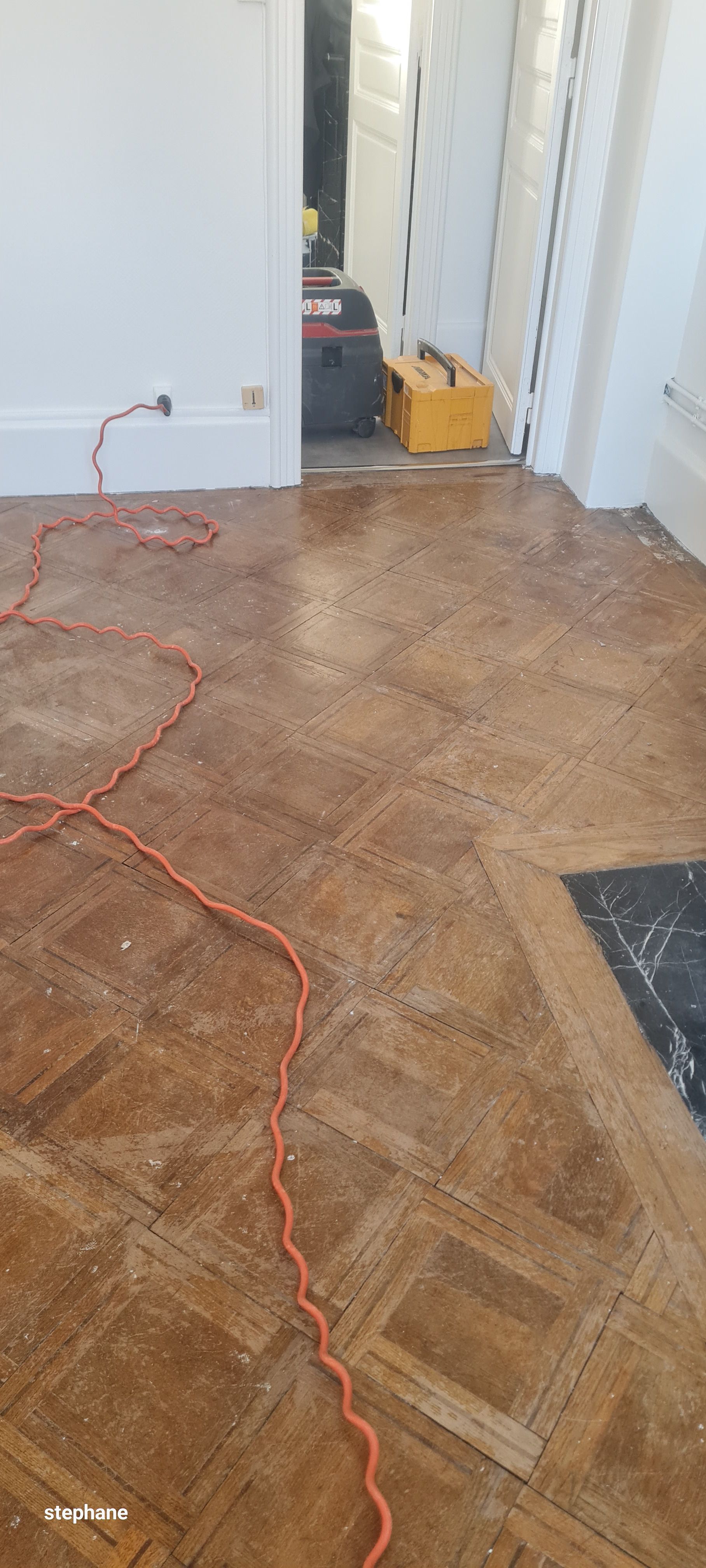 Sol en parquet dans une pièce avec un câble électrique orange. Outils dans l'encadrement de la porte