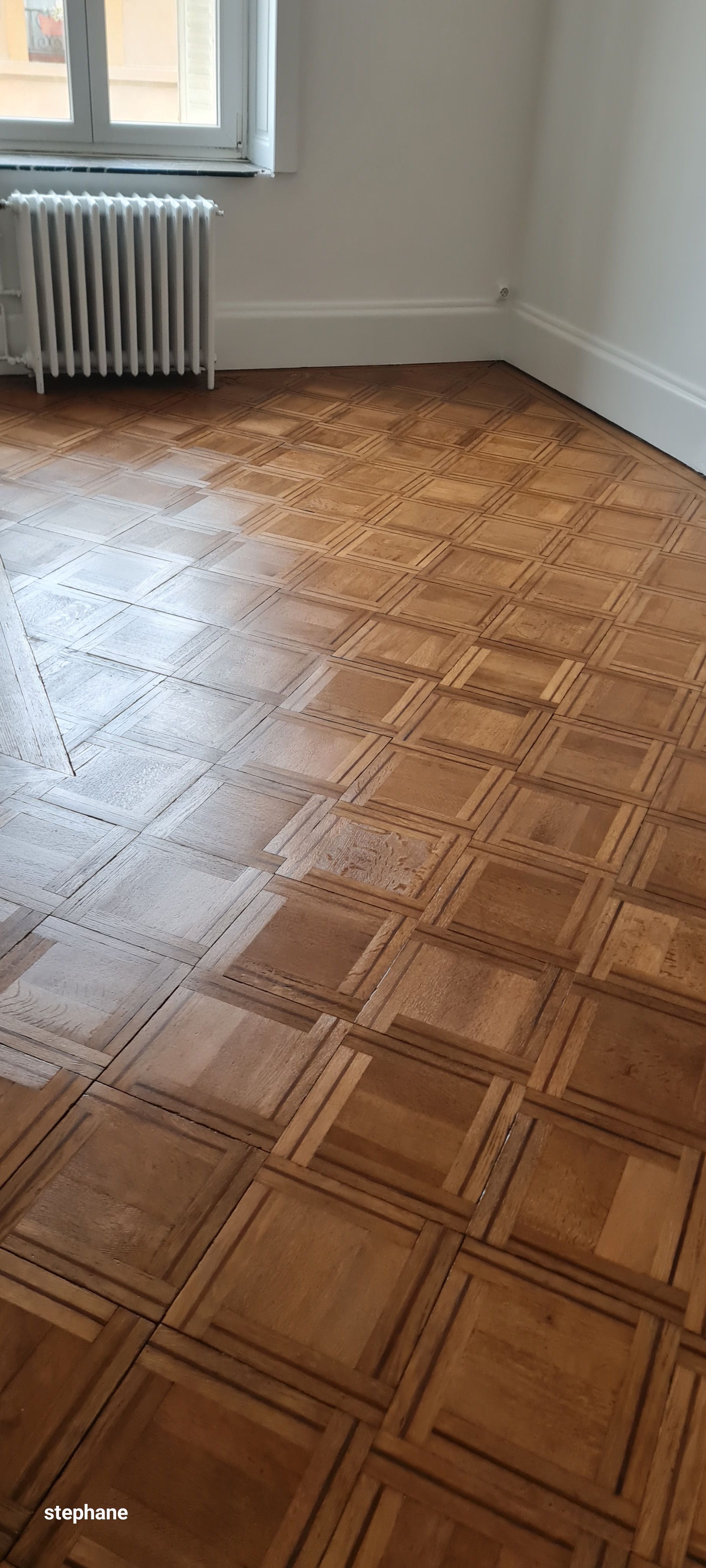 Parquet en bois dans une pièce avec radiateur et fenêtre, murs blancs et moulures