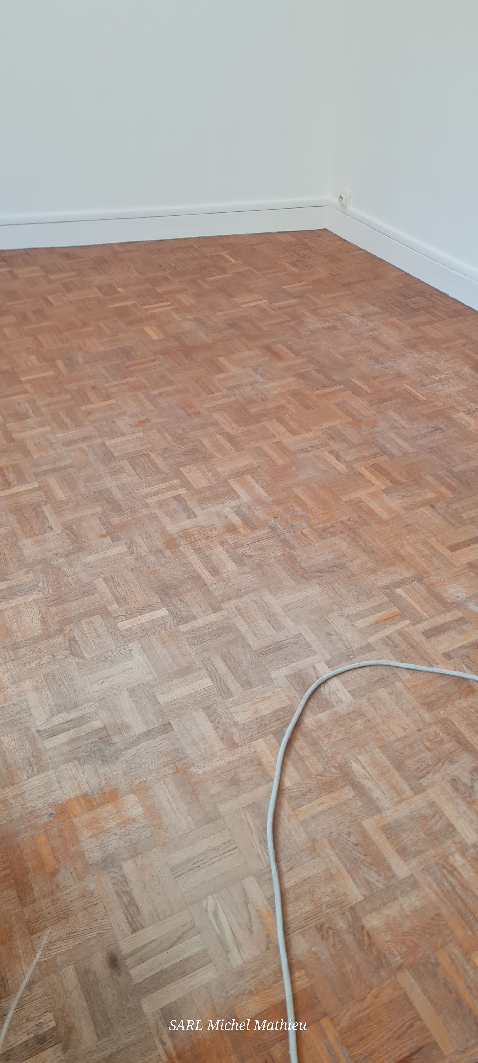 Parquet en bois dans une pièce aux murs blancs. Un câble est posé au sol