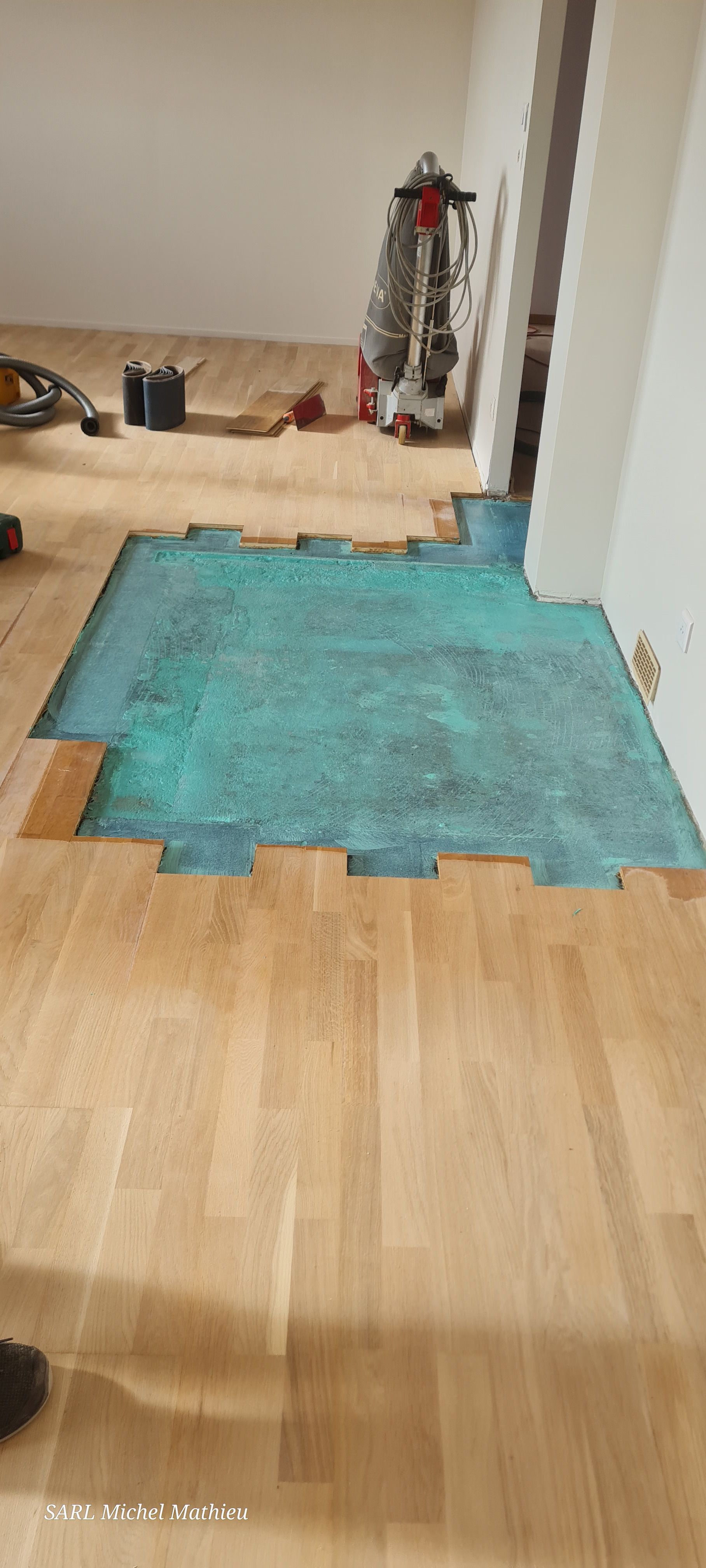 Plancher en bois partiellement installé, laissant apparaître une section de sous-couche bleue