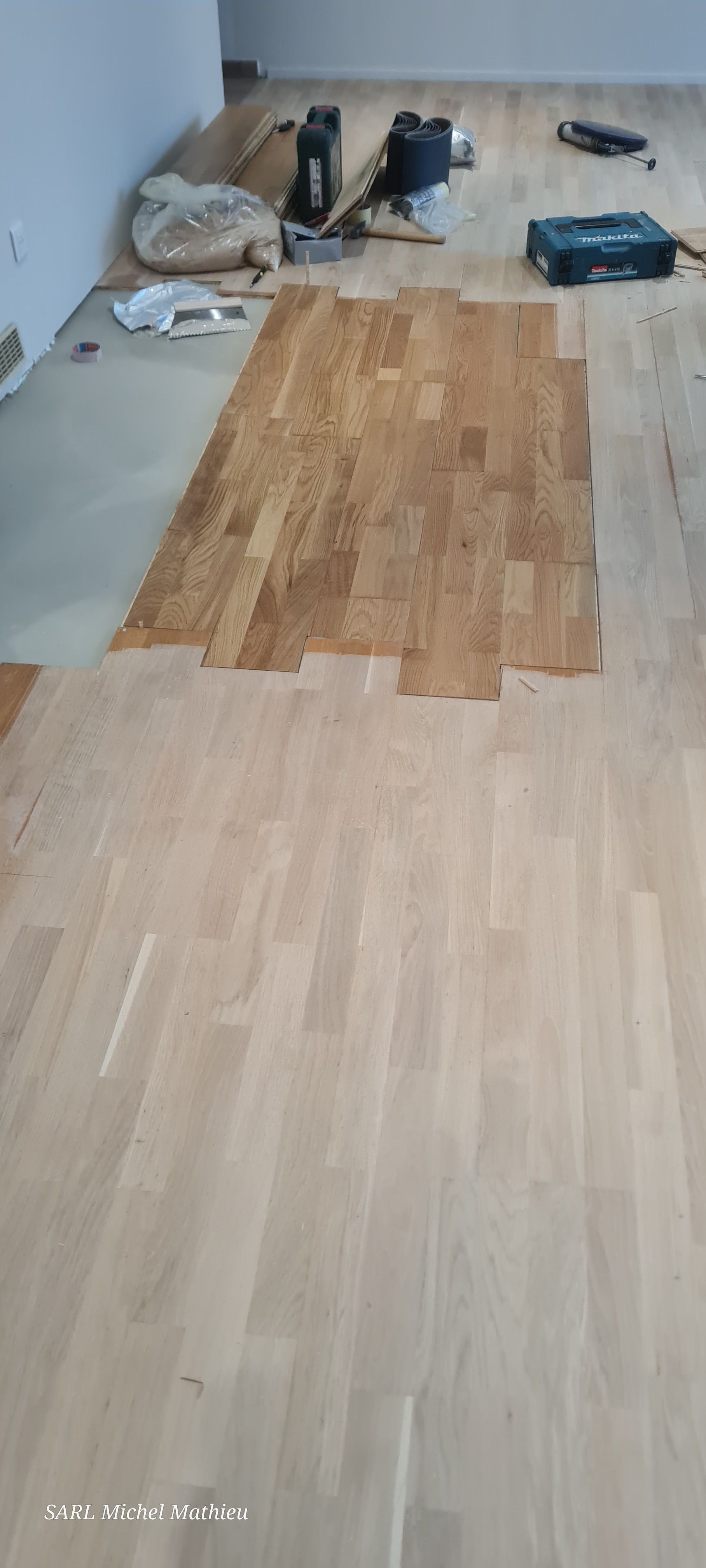 Pose d'un plancher en bois ; on aperçoit des outils et une partie du bois teinté