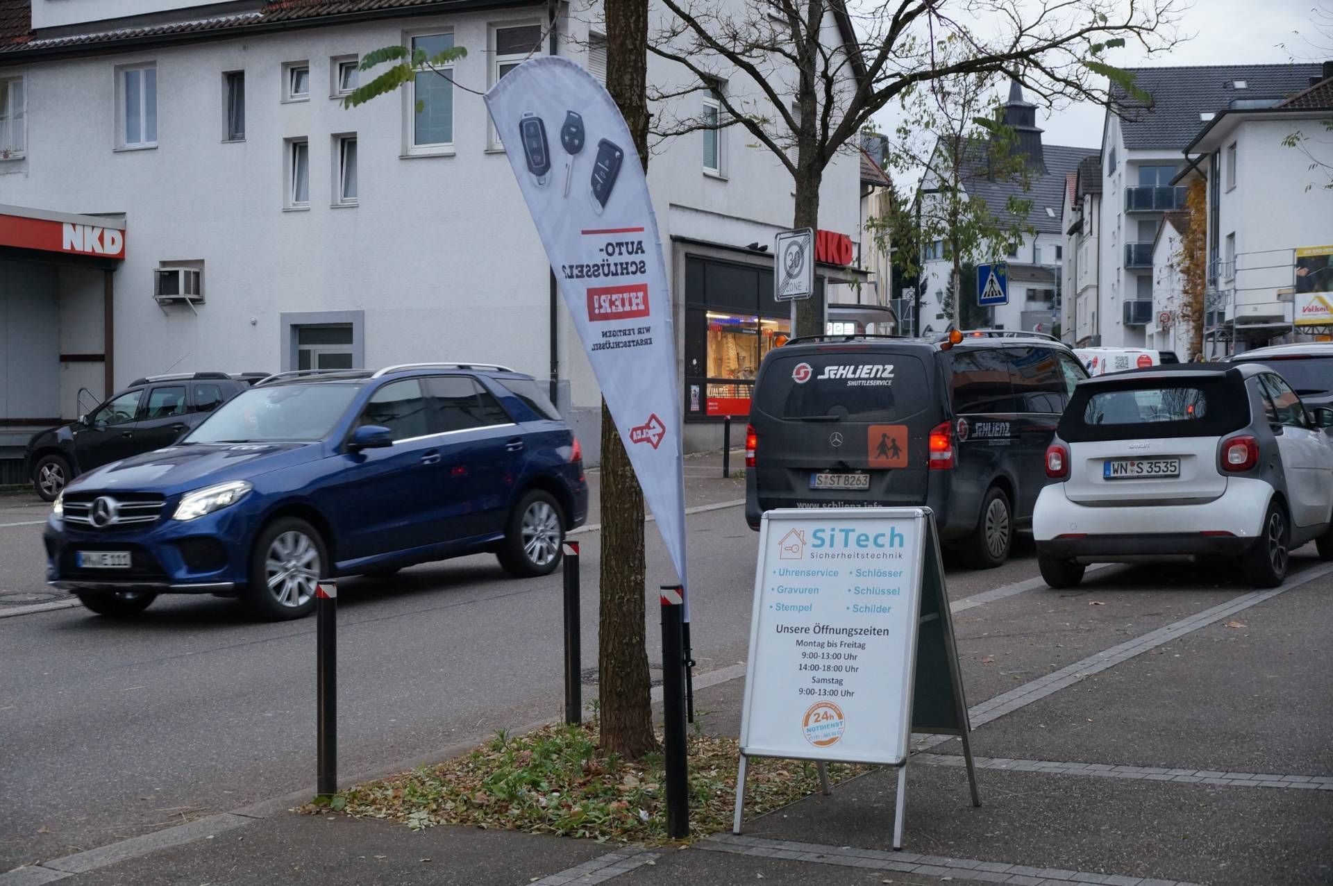 Eine Reihe Autos parkt am Straßenrand neben einem Schild mit der Aufschrift „SiTech“