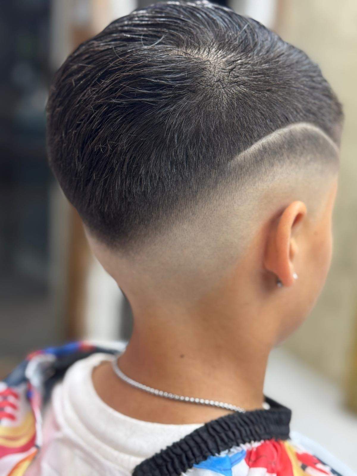 Niño con corte de pelo degradado, cabello oscuro en la parte superior, piel degradada en los costados y la espalda, con un diseño de líneas.